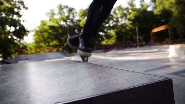 Man inline roller blader performing jumps at local skate park, Young gut on roller skates perform tricks on the ramp, freeze on the top then slide down. Extreme sports outdoors