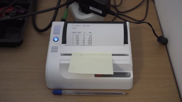 Thermal printer on messy desk prints summary of coin counting done by automatic coin counter.