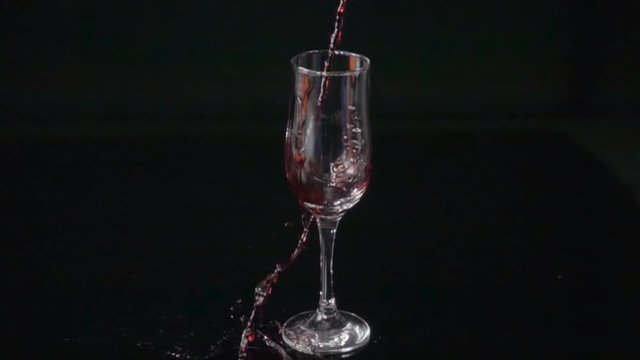 red wine pours by the glass in slow motion on black background