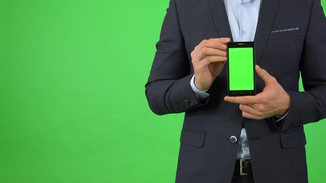 A businessman in a suit holds out a smartphone with green screen - closeup - green screen studio