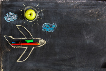 Back to school. Chalked drawing of an airplane on a school blackboard with school supplies and an...
