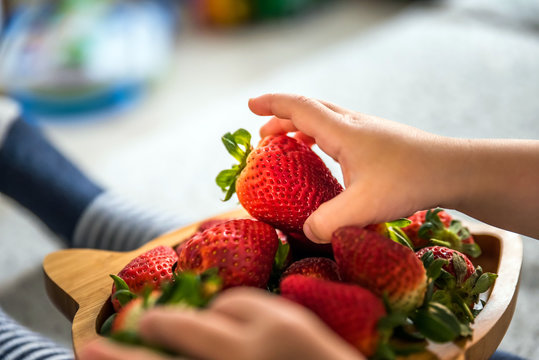 baby boy hands touch and take raw fresh strawberries on wooden bamboo plate indoor. baby exploring fruit - Powered by Adobe