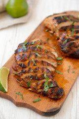 Grilled chipotle chicken breast on a rustic wooden board on a white wooden background, side view. Close-up.