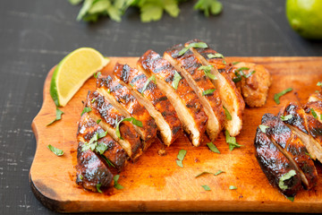 Grilled chipotle chicken breast on a rustic wooden board on a black surface, side view. Close-up.