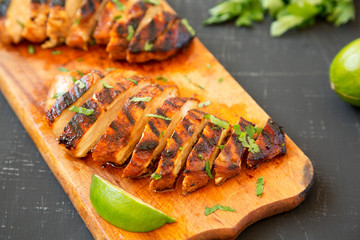 Grilled chipotle chicken breast on a rustic wooden board on a black surface, side view. Close-up.