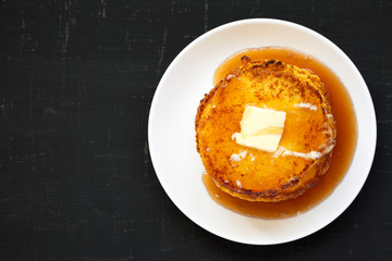 Homemade corn meal Johnny cakes on a white plate on a black surface, top view. Flat lay, overhead, from above. Copy space.