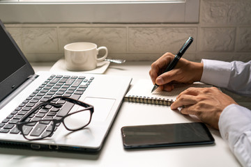 Businessman is taking a note on the notebook  from the financial imformation from laptop computer .business work concept.