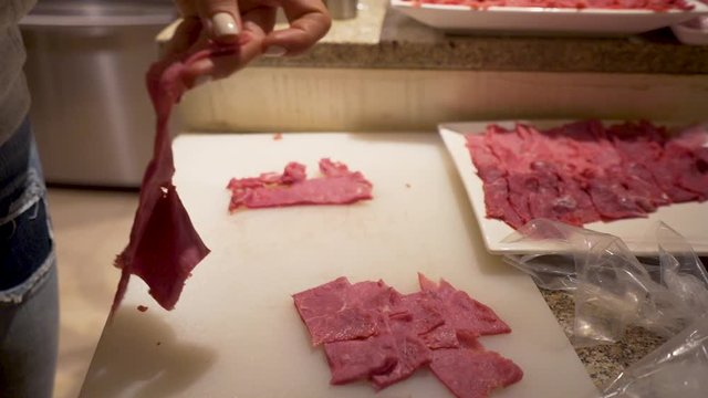 Slow Motion Close -up shot of a lady slicing thin beef meat steak strips on the kitchen counter using a sharp knife