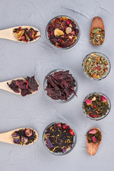 Assortment of aromatic tea, top view. Spoons and bowls with dried tea on gray background. Flat lay composition.