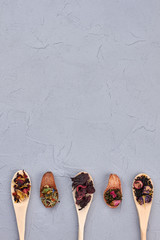 Spoons with tea leaves and copy space. Collection of wooden spoons with dried tea on gray background, top view.