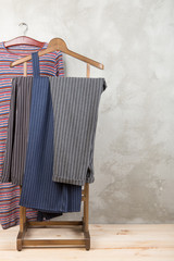 Shopping and style concept - clothes rack with trendy striped pants and dress on wooden floor and grey concrete background