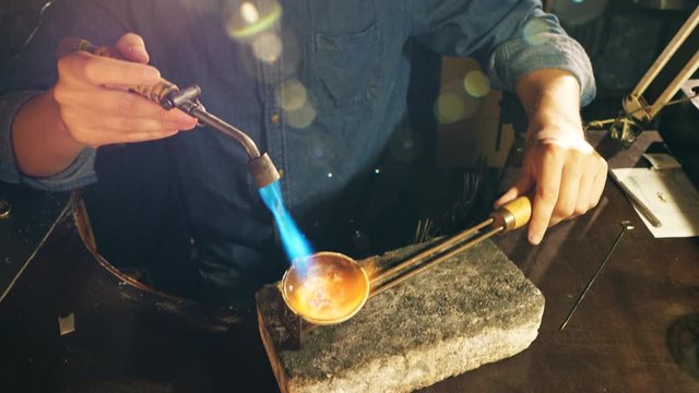 Jewelry is getting heated with the burner in craftsman's hands