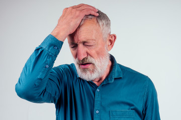 Elderly man with hand on his temple has a headache in studio white background