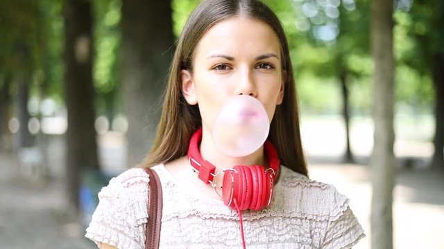 Outdoor lifestyle portrait of beautiful young woman blowing a bubble gum balloon