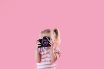 Little pretty girl photographer on pink background shooting with professional photo camera - obrazy, fototapety, plakaty