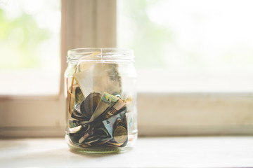 a glass bank with ash money coins and paper ones