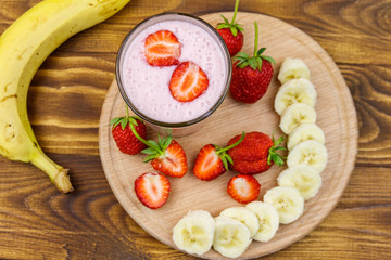 Glass of fresh smoothie of strawberry and banana on a wooden table. Top view