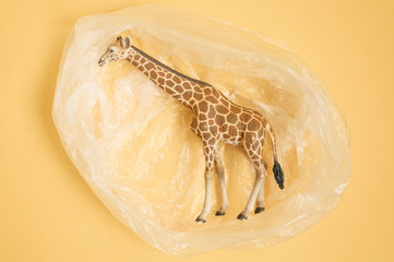 Concept for plastic pollution, environmental pollution, ecology problem. The figurine of a giraffe in a polyethylene bag. Children's toy. Flat lay, top view