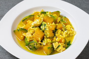 Fried pumpkin with egg for children in white dish on concrete table.