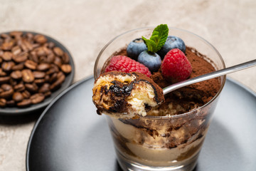 Classic tiramisu dessert portion with blueberries and raspberries in a glass cup on concrete background