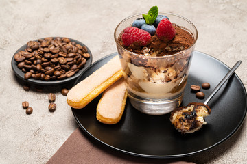 Classic tiramisu dessert portion with blueberries and raspberries in a glass cup on concrete background