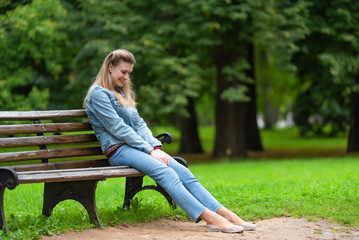 Young attractive smiling woman in casual jeans clothes resting on a park bench