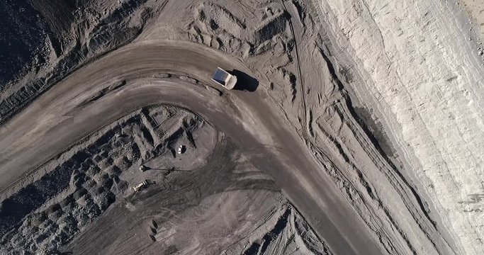 Deep open cut black coal mine in Hunter Valley area of NSW, Australia. Overhead top down aerial flying over moving trucks and excavators extracting coal.