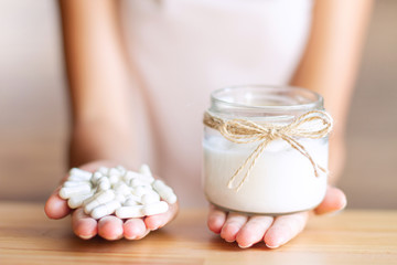 Obraz na płótnie Canvas Female hands are holding capsules with bifidobacteria in left hand and natural yogurt in right. Young woman makes choice between pills and dairy products. Nutrition that promotes good digestion.