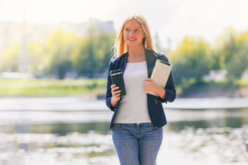 Young happy smiling caucasian adult girl business student walking concept in the summer green park outdoor holding tablet and coffee thinking of credit money finance people job in the college