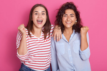 Portrait of young women wearing casual clothes standing and looking camera, fameles keeping mouth open, clenching fists isolated on bright pink background in studio. People lifestyle concept.