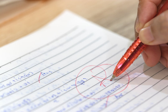 Concept of measurement and evaluation. Hand of teacher using red pen written grade A and circle on math exam paper on wood desk.