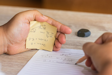 Student using formula math sheet to cheat on test. Hand of university student holding pencil doing...