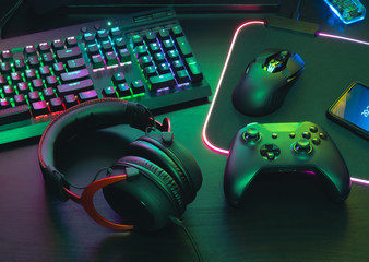 gamer work space concept, top view a gaming gear, mouse, keyboard, joystick, headset, mobile joystick, in ear headphone and mouse pad on black table background.