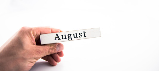 August - A hand holding calendar month block on white background