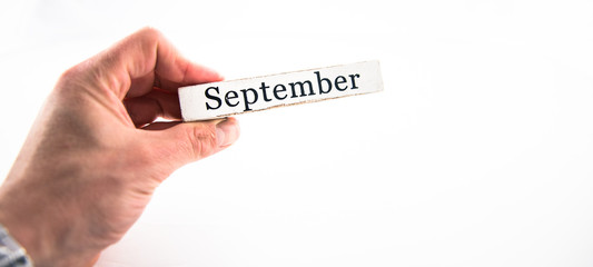 September - A hand holding calendar month block on white background