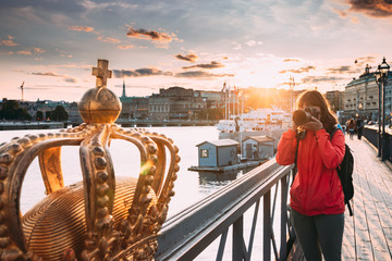 Stockholm, Sweden. Young Caucasian Woman Lady Tourist Traveler Photographer Taking Pictures Photos Of Golden Crown On Skeppsholmsbron - Skeppsholm Bridge. Famous Popular Place Landmark Destination