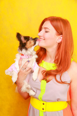 Cute pretty young lady wearing stylish bright summer dress and smiling while hugging adorable little puppy Papillon on white studio background