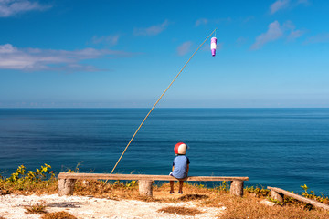 Dreaming boy sits on a bench in a helmet on the background of the sea. View point