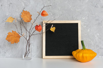 Fototapeta na wymiar Blank black letter board frame and Autumn bouquet of branches with yellow leaves on clothespins in vase, patisson on table Mockup Template for your text, greeting card Concept Hello autumn