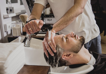 Young man with trendy haircut at barber shop. Barber washes customer head.