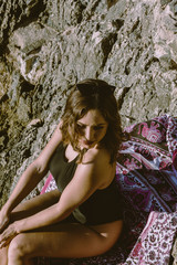 Naklejka premium Young hipster woman lying on the rocks in a swimsuit over beach towel. Young woman lying near the sea with vintage sunglasses.