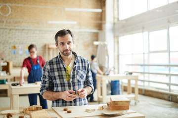 Portrait of mature carpenter working with wood in workshop and looking at camera, copy space