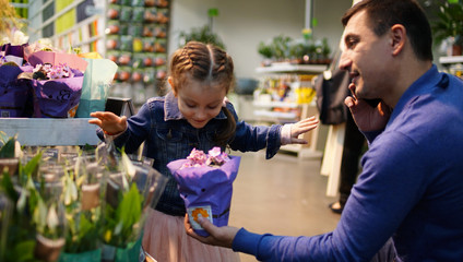 Portrait of cute little girl with dad giving bouquet of flowers in supermarket