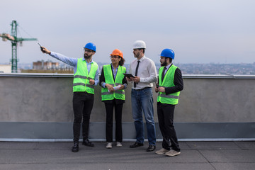 A group of multiethnic workers at construction site engineer architects and foreman analyzing the plan of construction site using a tablet and wearing safety helmets