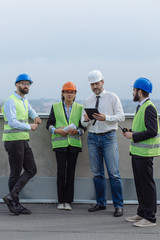 Multiethnic group of workers engineers architects foreman analyzing the plan of construction site on the rooftop of modern building.