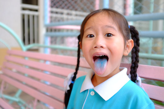 Funny Face Little Asian Child Girl Smile And Poking Out Blue Colored Tongue. Food Coloring In Children Sweets.