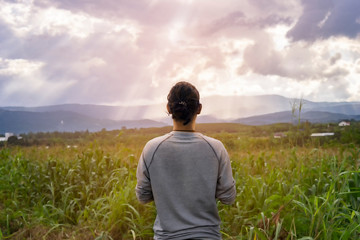 Fototapeta premium Enjoying the nature standing in landscape at sunset watching The light shining from the clouds. female looking at sunset on the horizon