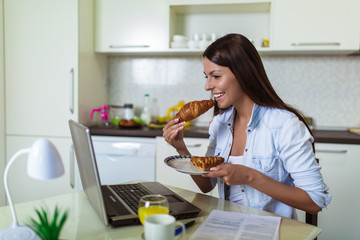 Attractive young woman working with laptop computer and documents while sitting at the kitchen.