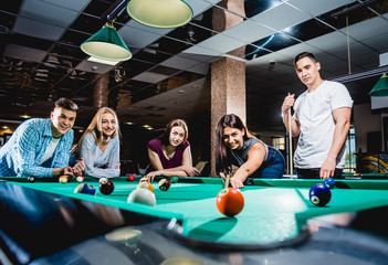 Group of young cheerful friends playing billiards.
