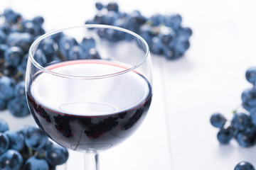glass of red wine and blue grapes on white wooden table background